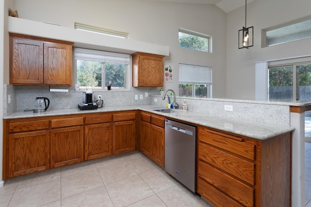 kitchen with brown cabinets, a peninsula, hanging light fixtures, stainless steel dishwasher, and a sink