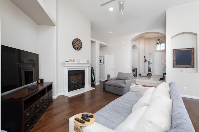 living room with baseboards, arched walkways, a glass covered fireplace, dark wood-type flooring, and recessed lighting