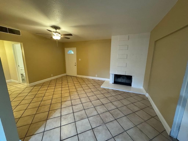 unfurnished living room with a textured ceiling, ceiling fan, a large fireplace, and light tile patterned floors