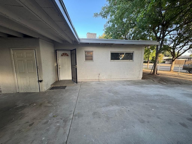entrance to property featuring stucco siding, fence, and a patio