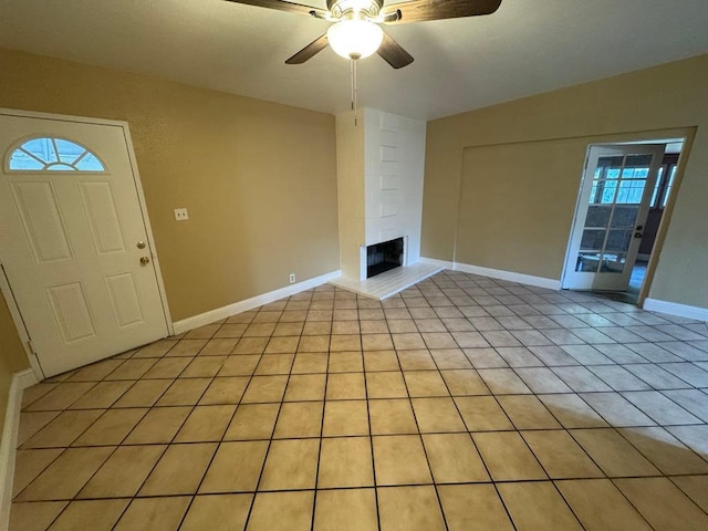 unfurnished living room with a wealth of natural light, a fireplace, light tile patterned floors, and ceiling fan