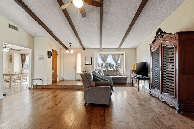 living area with wood-type flooring, ceiling fan with notable chandelier, a textured ceiling, and visible vents