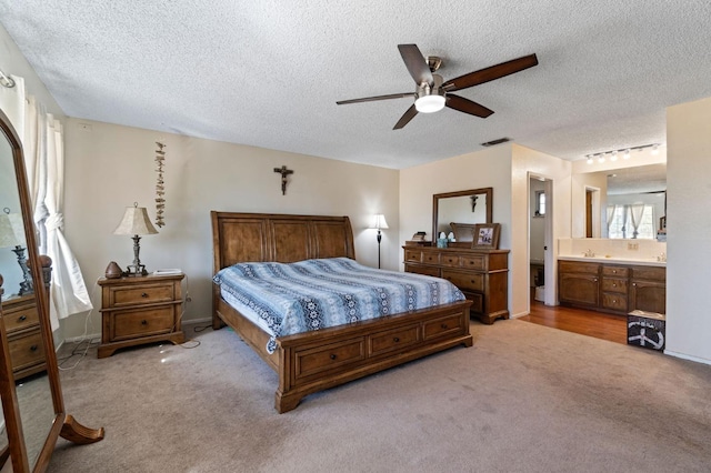 bedroom featuring ceiling fan, a textured ceiling, visible vents, connected bathroom, and light carpet