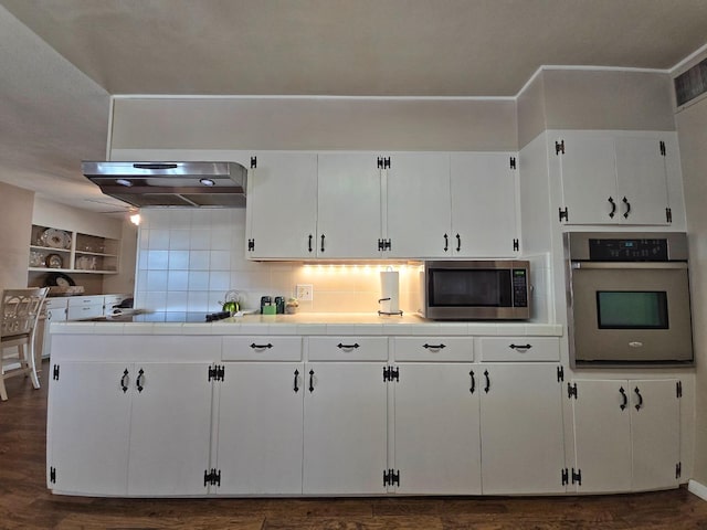 kitchen featuring appliances with stainless steel finishes, white cabinetry, tile counters, decorative backsplash, and exhaust hood