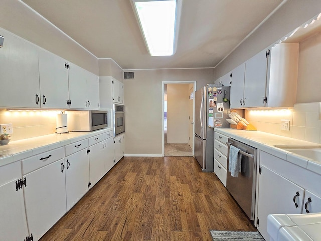 kitchen featuring appliances with stainless steel finishes, white cabinetry, backsplash, dark hardwood / wood-style floors, and tile counters