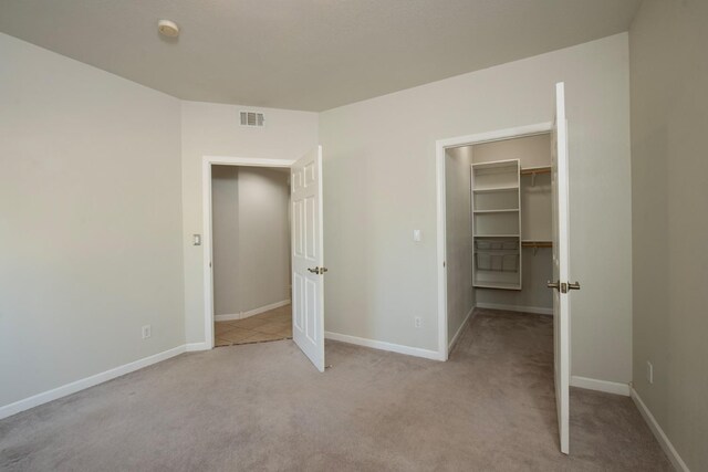 unfurnished bedroom with a spacious closet, light carpet, and a closet