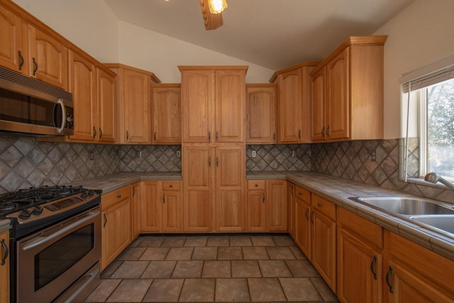 kitchen with backsplash, vaulted ceiling, sink, tile counters, and stainless steel appliances