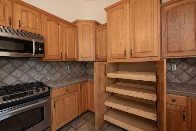 kitchen featuring tile countertops, stainless steel appliances, backsplash, and dark tile patterned flooring