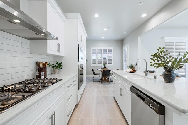 kitchen featuring sink, stainless steel appliances, wall chimney exhaust hood, white cabinets, and light stone counters