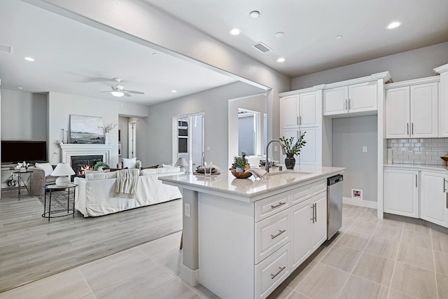 kitchen featuring backsplash, ceiling fan, stainless steel dishwasher, white cabinets, and a center island with sink