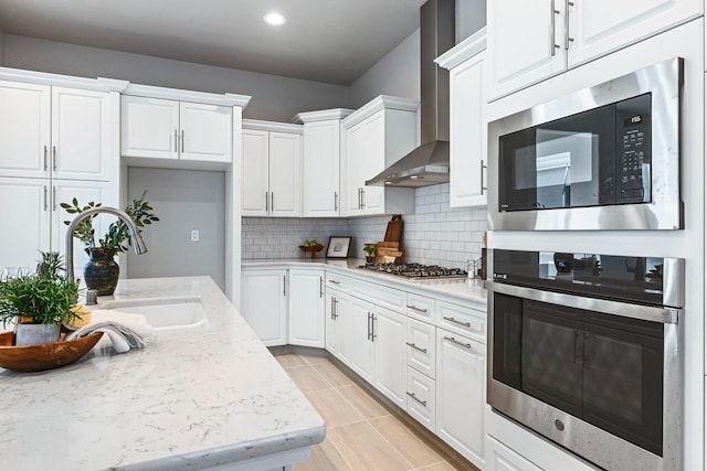 kitchen with wall chimney range hood, decorative backsplash, light tile patterned floors, white cabinetry, and stainless steel appliances