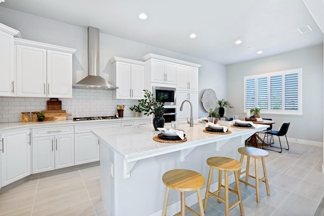 kitchen featuring wall chimney exhaust hood, white cabinetry, tasteful backsplash, and a center island with sink