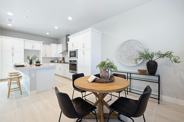 kitchen with a kitchen island, appliances with stainless steel finishes, a kitchen breakfast bar, white cabinetry, and wall chimney exhaust hood