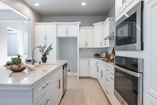 kitchen with white cabinets, stainless steel appliances, sink, and light stone counters