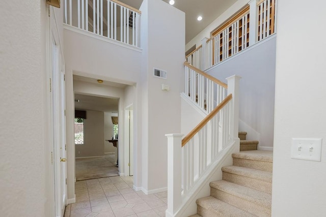 staircase with a towering ceiling and tile patterned flooring