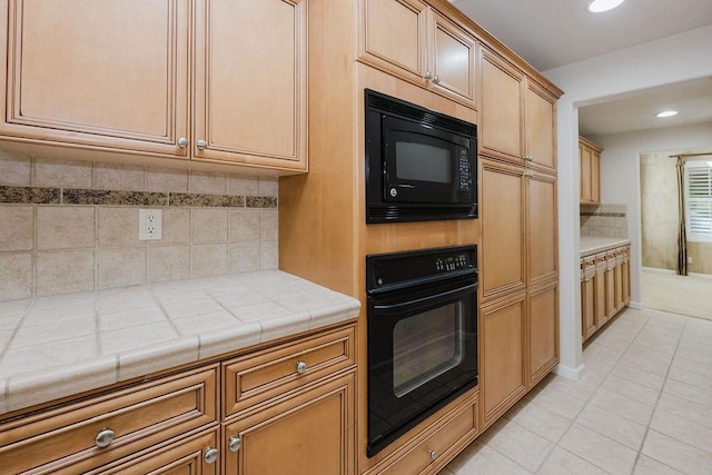 kitchen with tile countertops, backsplash, light tile patterned floors, and black appliances