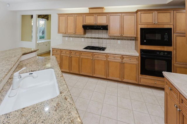 kitchen with backsplash, light stone countertops, sink, and black appliances