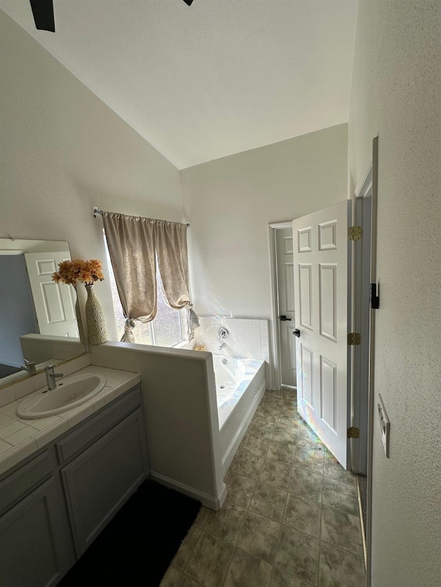 bathroom featuring vanity, a tub to relax in, and vaulted ceiling