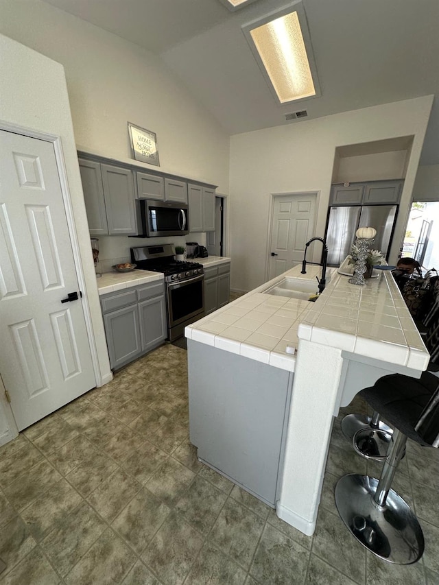 kitchen with appliances with stainless steel finishes, sink, vaulted ceiling, tile counters, and gray cabinets