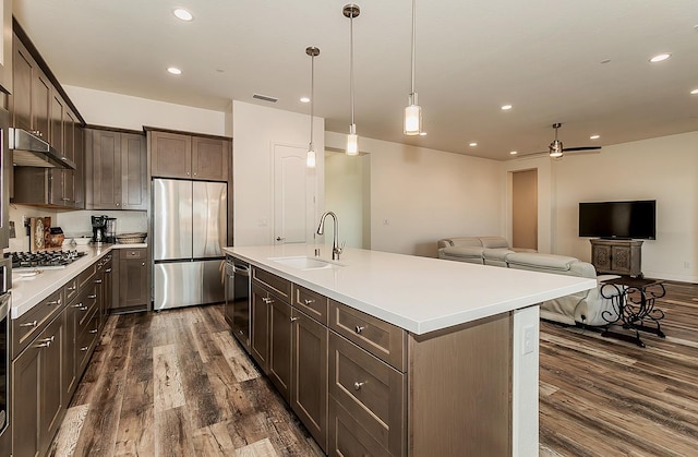 kitchen with a kitchen island with sink, dark wood-type flooring, stainless steel appliances, sink, and dark brown cabinetry