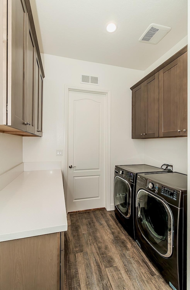 clothes washing area with washing machine and dryer, dark hardwood / wood-style floors, and cabinets