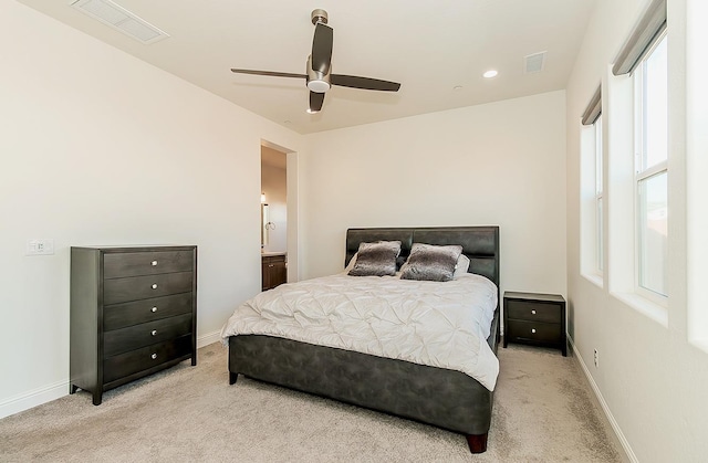 bedroom with connected bathroom, light carpet, multiple windows, and ceiling fan