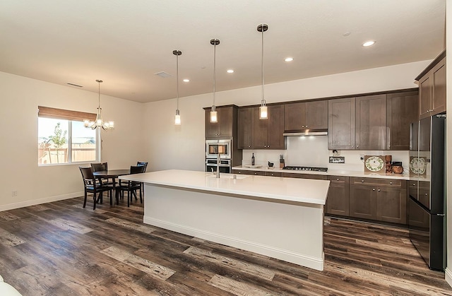 kitchen featuring appliances with stainless steel finishes, an island with sink, dark brown cabinetry, pendant lighting, and dark hardwood / wood-style floors