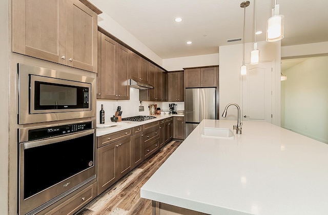 kitchen with hardwood / wood-style floors, dark brown cabinets, hanging light fixtures, sink, and stainless steel appliances