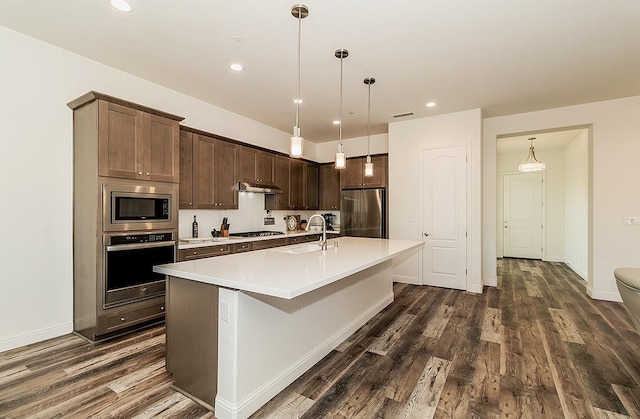 kitchen with hanging light fixtures, a kitchen island with sink, dark hardwood / wood-style floors, sink, and stainless steel appliances