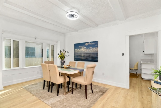 dining space featuring beam ceiling, light hardwood / wood-style flooring, and a textured ceiling