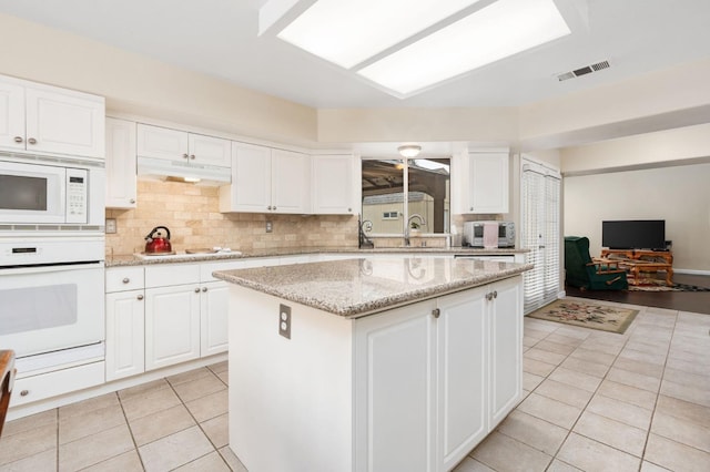 kitchen with white cabinetry, sink, light tile patterned flooring, white appliances, and a kitchen island