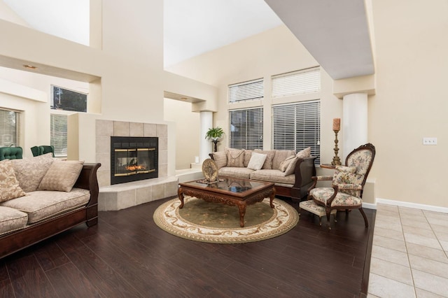 living room featuring wood-type flooring, a tile fireplace, and a towering ceiling