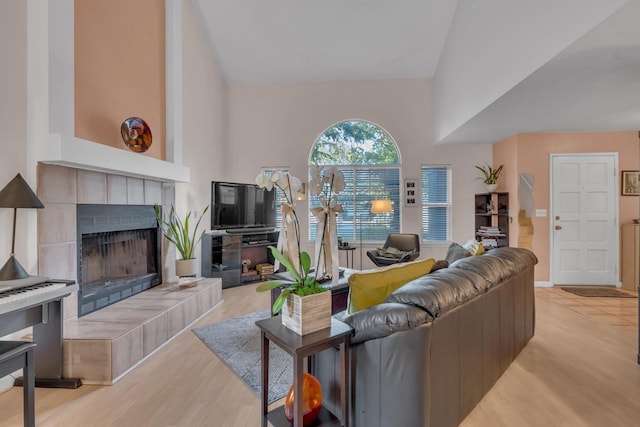 living room featuring high vaulted ceiling, a fireplace, and light wood-type flooring