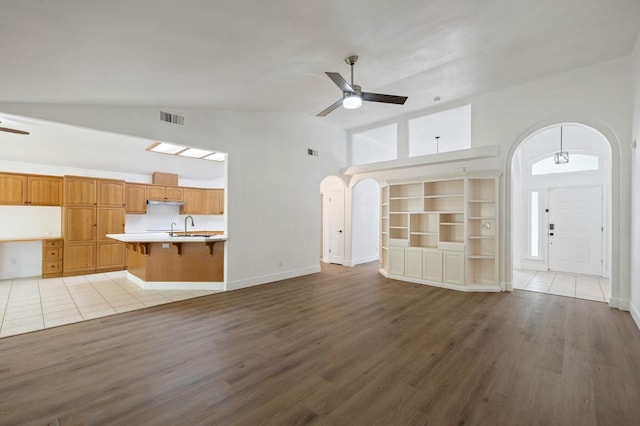 unfurnished living room with light hardwood / wood-style floors, high vaulted ceiling, sink, and ceiling fan