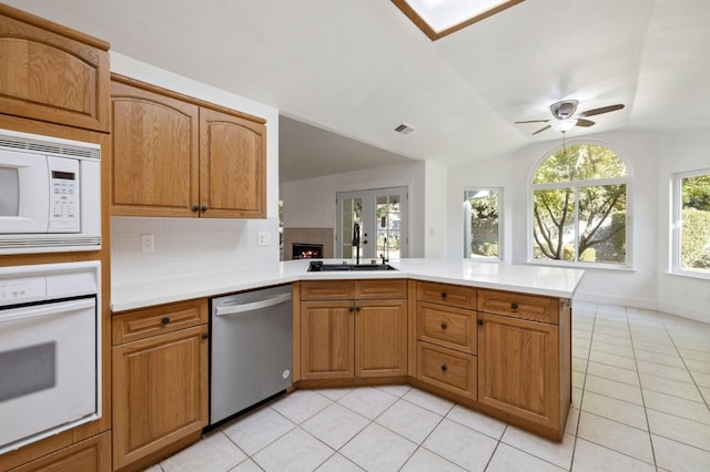 kitchen featuring kitchen peninsula, a healthy amount of sunlight, white appliances, and vaulted ceiling