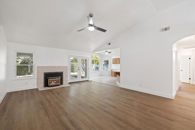 unfurnished living room featuring french doors, a tiled fireplace, hardwood / wood-style flooring, and a wealth of natural light