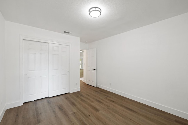 unfurnished bedroom featuring a closet, a textured ceiling, and dark wood-type flooring