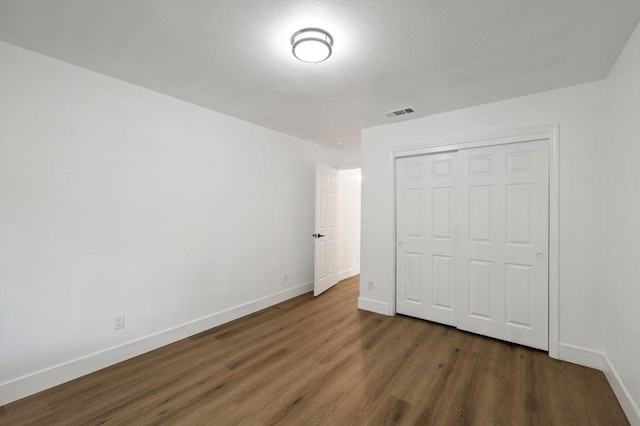 unfurnished bedroom featuring a textured ceiling, dark hardwood / wood-style floors, and a closet