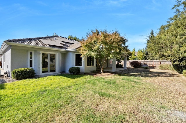 back of property with a yard, a patio, and solar panels