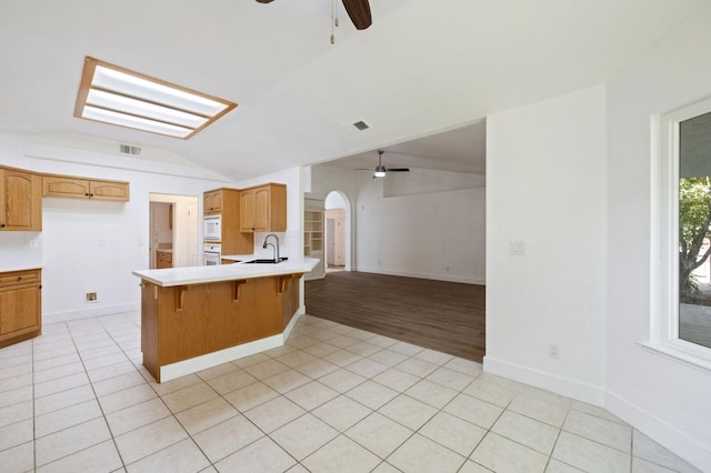 kitchen featuring kitchen peninsula, a kitchen bar, light hardwood / wood-style flooring, vaulted ceiling with skylight, and white appliances