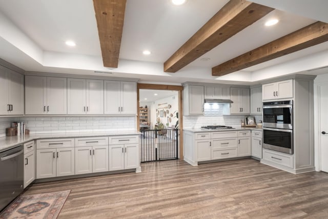 kitchen with beamed ceiling, stainless steel appliances, light wood-type flooring, and backsplash