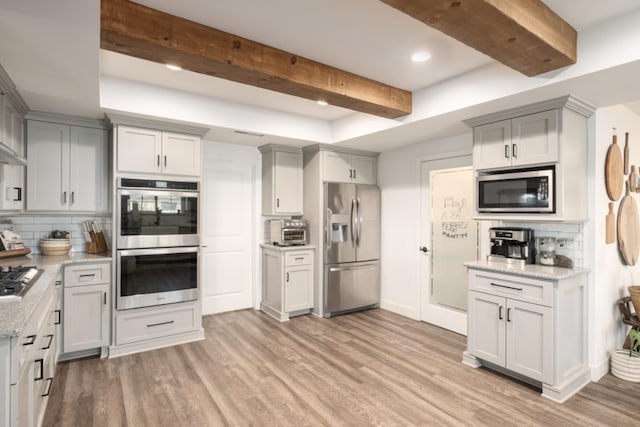 kitchen with decorative backsplash, beam ceiling, light stone countertops, light wood-type flooring, and appliances with stainless steel finishes