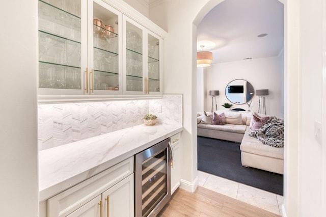 bar featuring white cabinets, light hardwood / wood-style floors, light stone countertops, and beverage cooler