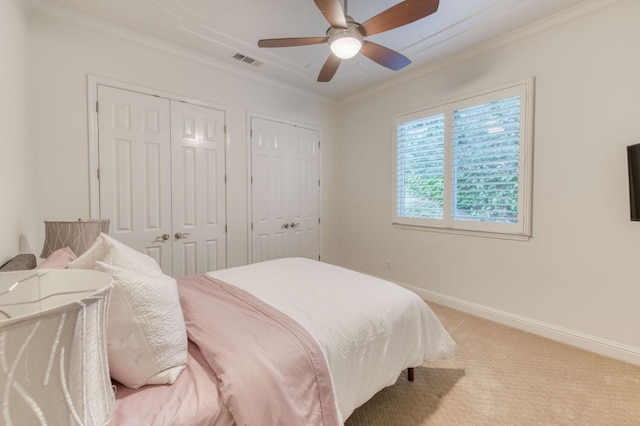 carpeted bedroom featuring ceiling fan, crown molding, and two closets