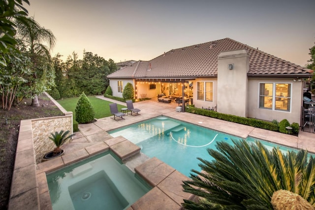 pool at dusk with a patio and an in ground hot tub