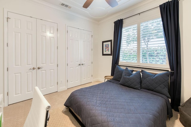 carpeted bedroom featuring multiple closets, ornamental molding, and ceiling fan