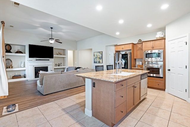 kitchen featuring an island with sink, appliances with stainless steel finishes, light wood-type flooring, built in shelves, and sink