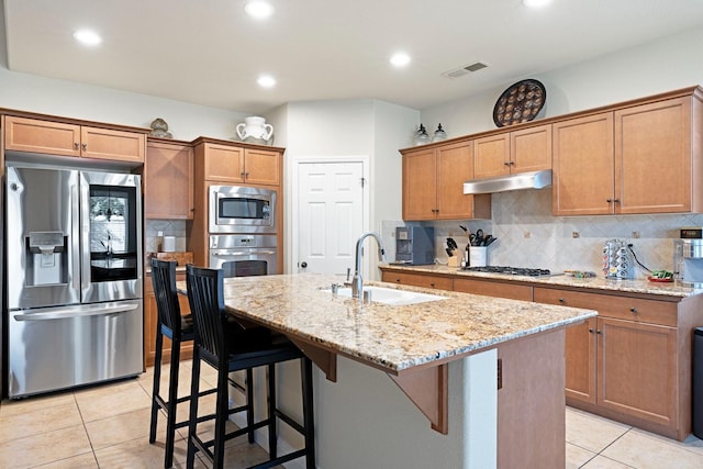 kitchen featuring light stone countertops, appliances with stainless steel finishes, sink, a breakfast bar area, and a kitchen island with sink