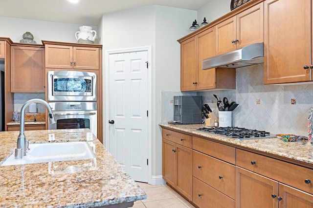 kitchen with sink, light stone countertops, light tile patterned flooring, appliances with stainless steel finishes, and tasteful backsplash