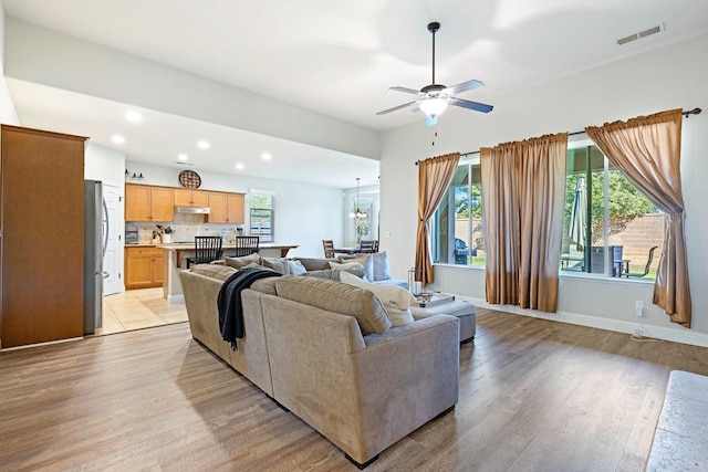 living room with light wood-type flooring and ceiling fan with notable chandelier